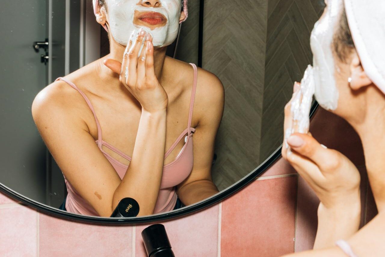 A woman applying cleansing foam on her face while looking at the mirror in a bathroom