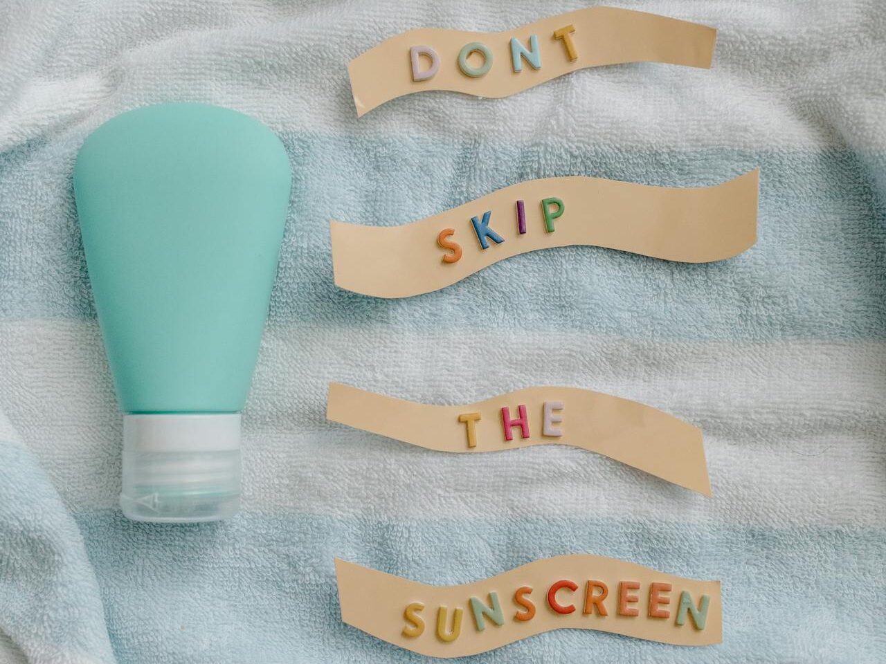 a sunscreen bottle and words 'don't skip the sunscreen' placed on a skyblue colored towel